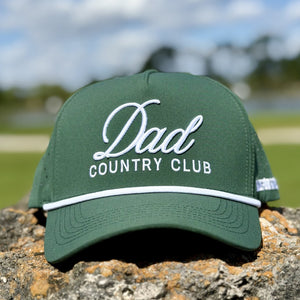 Green cap with 'Dad Country Club' text on a stone surface with a blurred natural background
